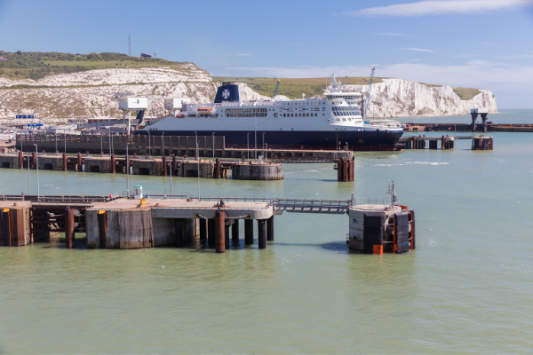 Eine Fähre von DFDS am Kai im Hafen von Dover, dahinter die weißen Klippen, im Vordergrund Betondalben im grünen Wasser