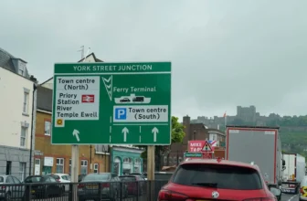 Verkehr durch Dover in Richtung der Fähre, mit einem grünen Verkehrsschild im Vordergrund und der Burg auf dem Hügel im Hintergrund.