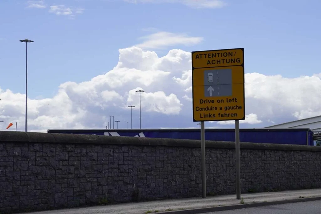 Verkehrsschild am Straßenrand beim Hafen, das darauf hinweist, dass es wichtig ist, links zu fahren.