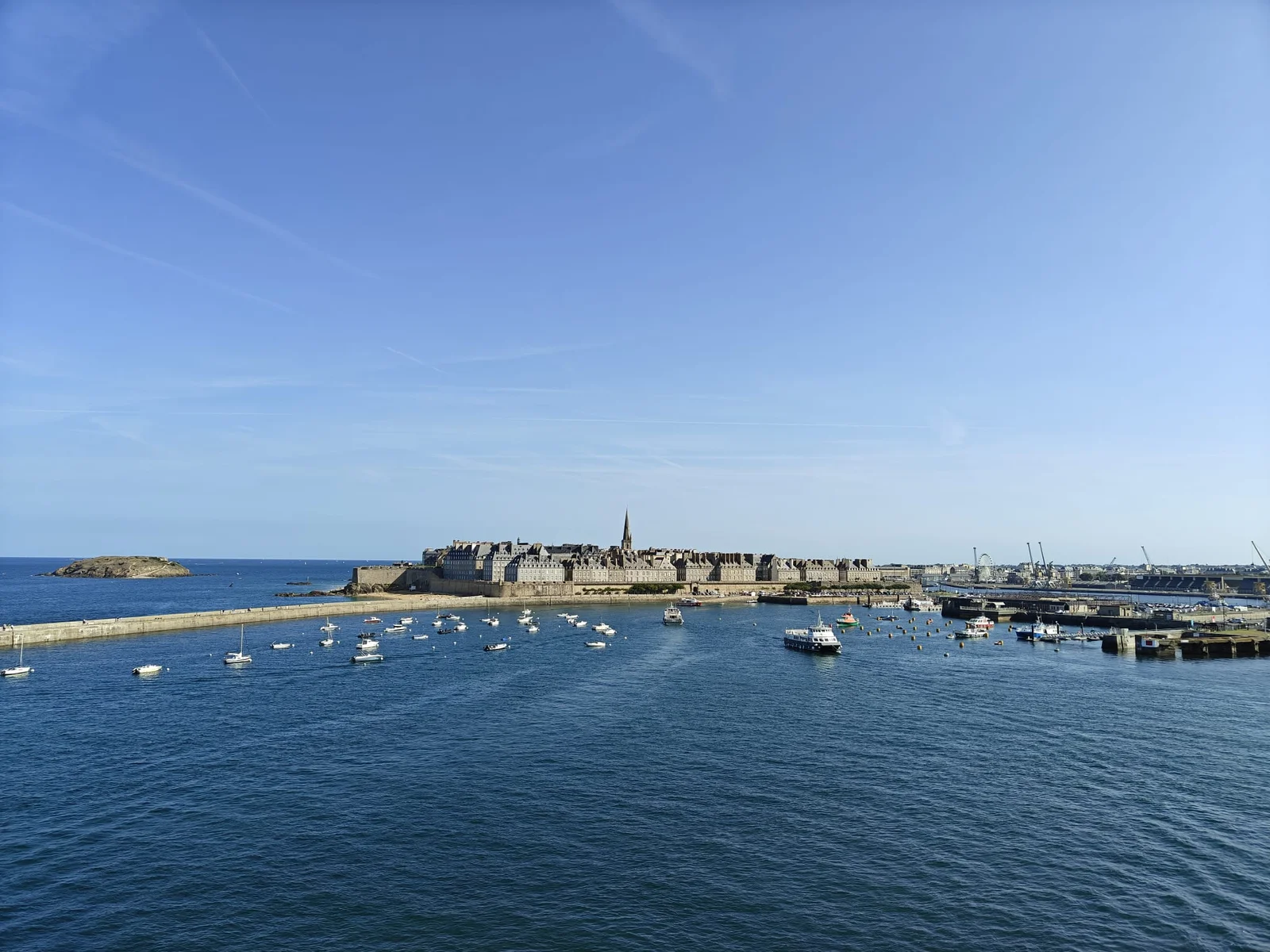 Die ummauerte Stadt Saint-Malo mit dem Turm der Kathedrale, gesehen vom Deck der auslaufenden Fähre, mit Dutzenden Booten auf dem Wasser davor