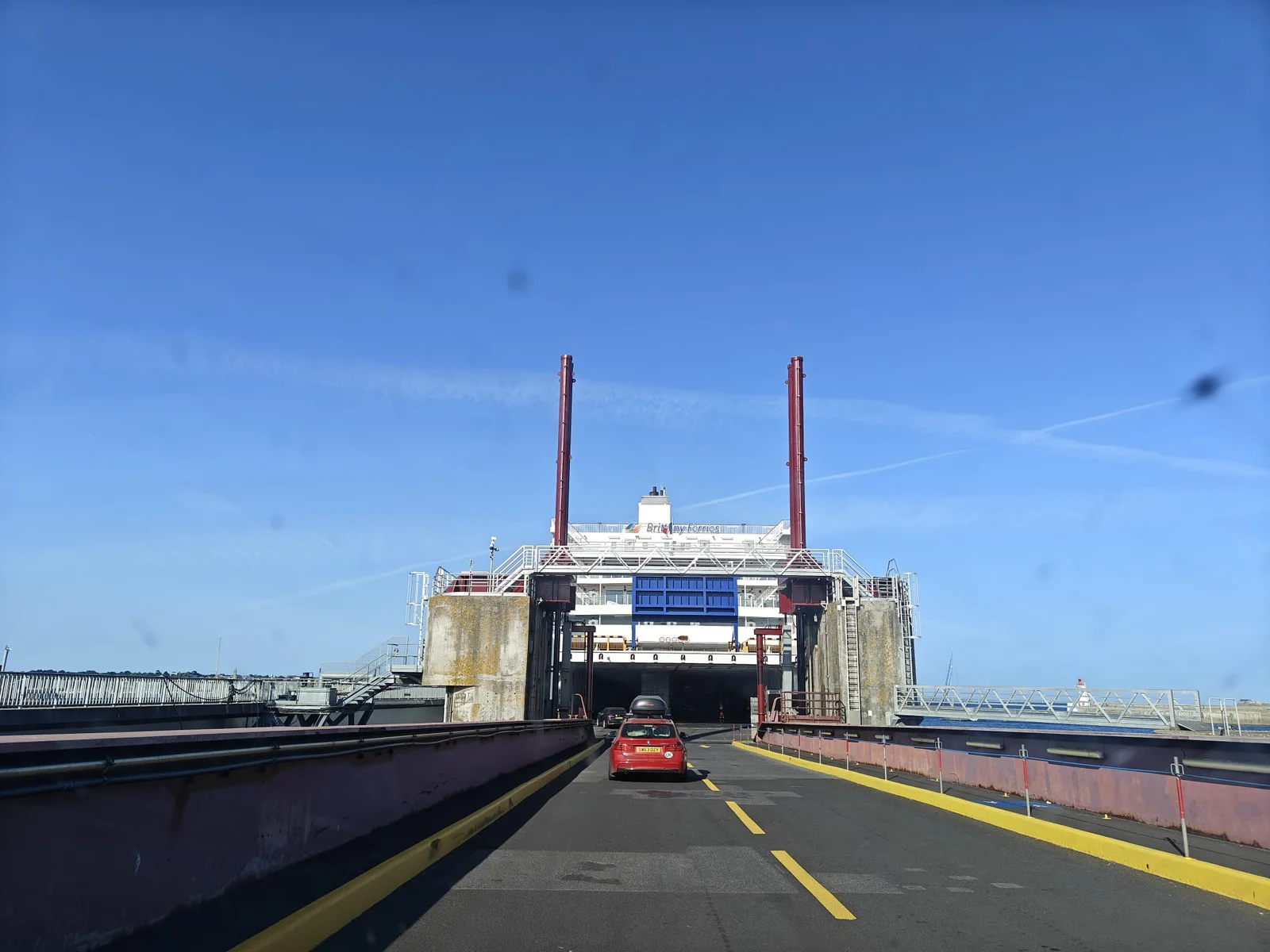 Ein rotes Auto fährt über die Rampe in den offenen Bug einer weißen Fähre von Brittany Ferries, unter strahlend blauem Himmel im Hafen von Saint-Malo