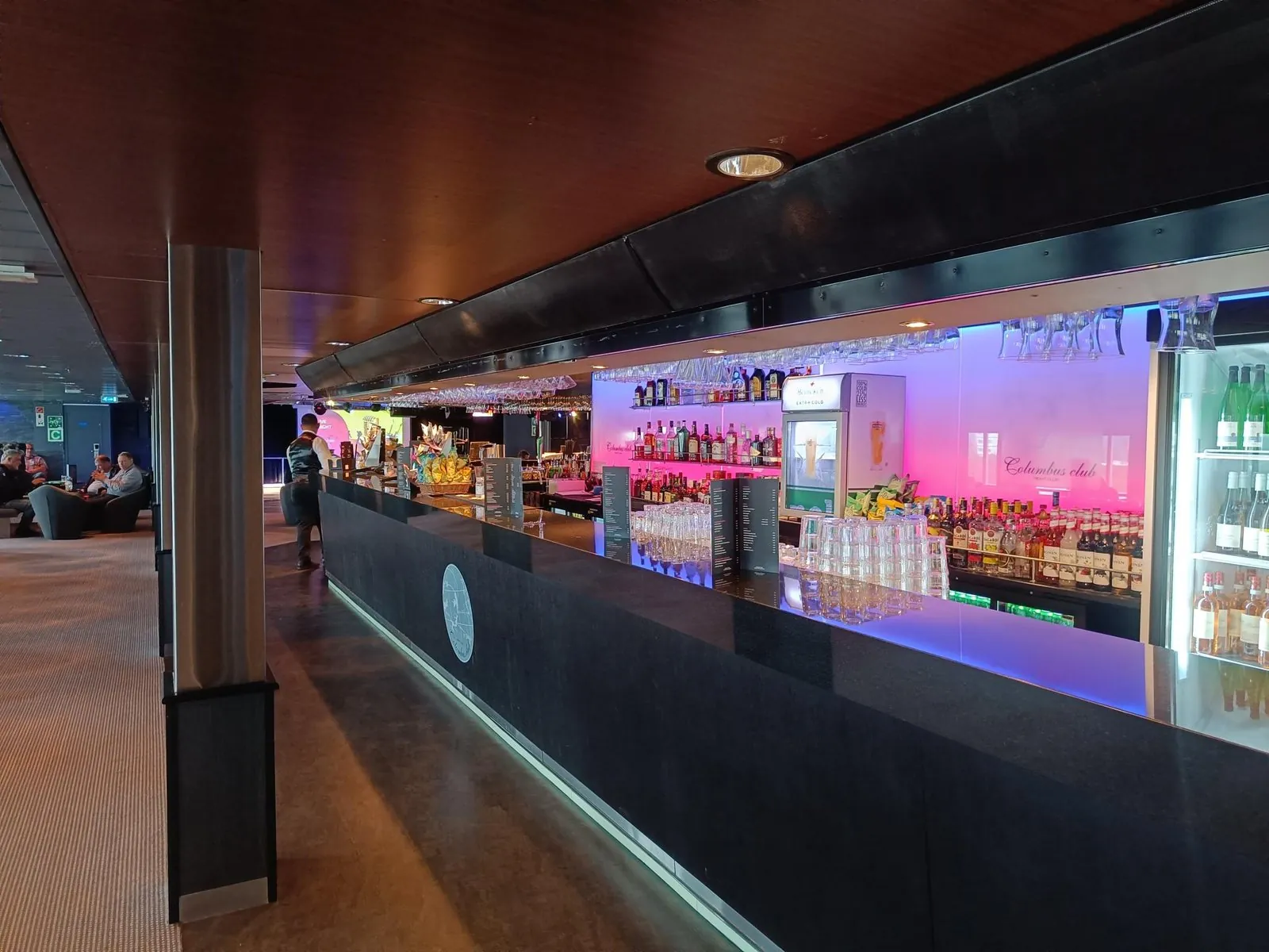 Die lange Bar an Bord mit einer beleuchteten Flaschenwand und Gläsern an der Decke; auf dem Glas dahinter steht Columbus Club