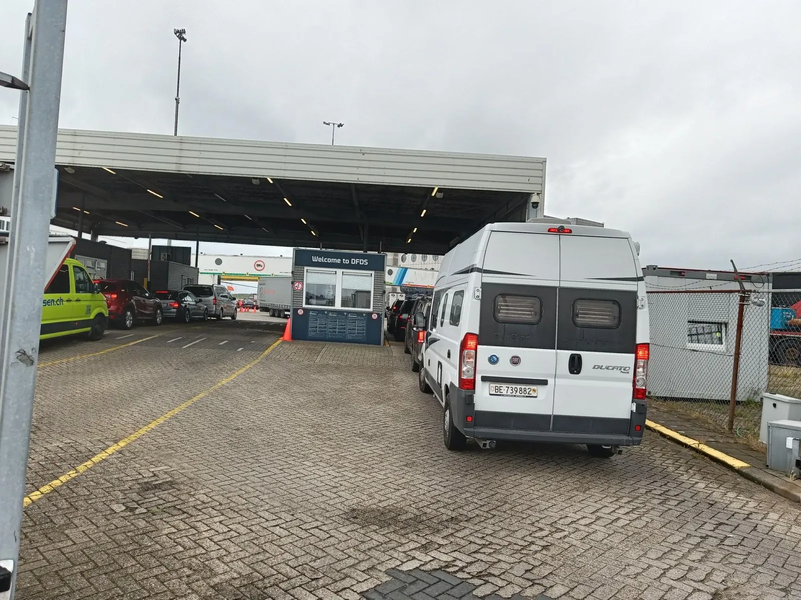 Autos und ein Wohnmobil in der Schlange vor der Kontrollstelle unter dem Dach in IJmuiden, mit Welcome to DFDS am Häuschen