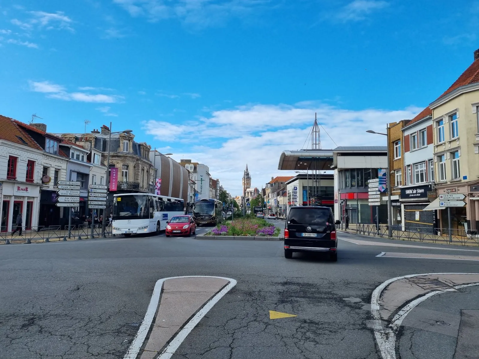 Kreuzung im Zentrum von Calais mit französischen Wegweisern zu Hôtel de Ville, Gare und Port Car Ferry, zwei Bussen und im Hintergrund dem Belfried