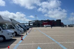 Wohnmobile und Transporter in der Warteschlange auf dem Terminalgelände, mit dem Schnellschiff Fjord FSTR im Hintergrund