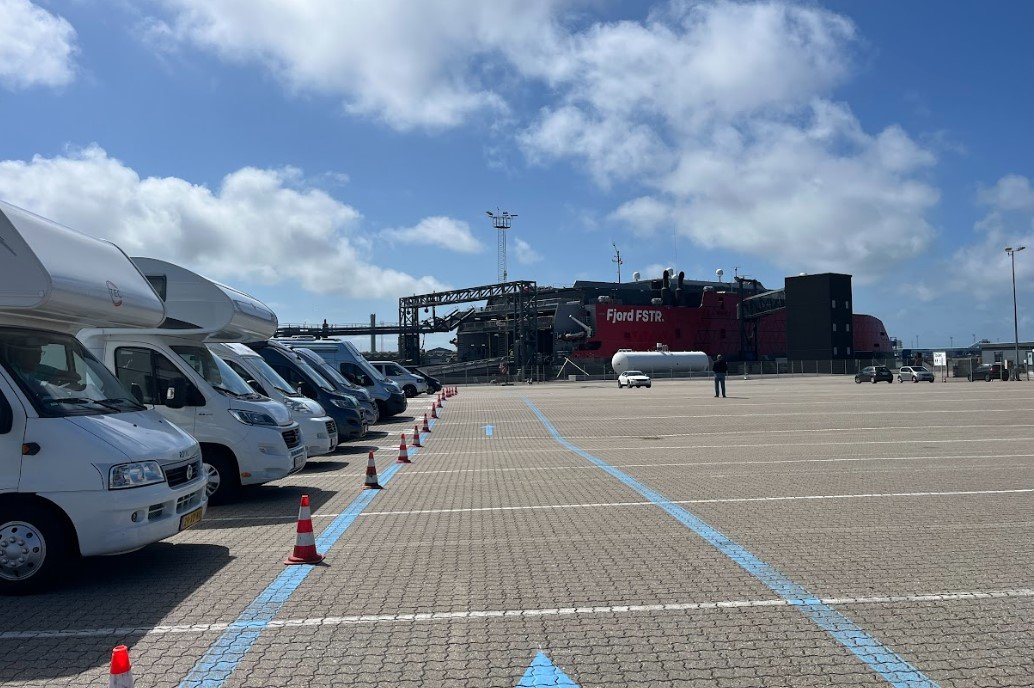 Wohnmobile und Transporter in der Warteschlange auf dem Terminalgelände, mit dem Schnellschiff Fjord FSTR im Hintergrund