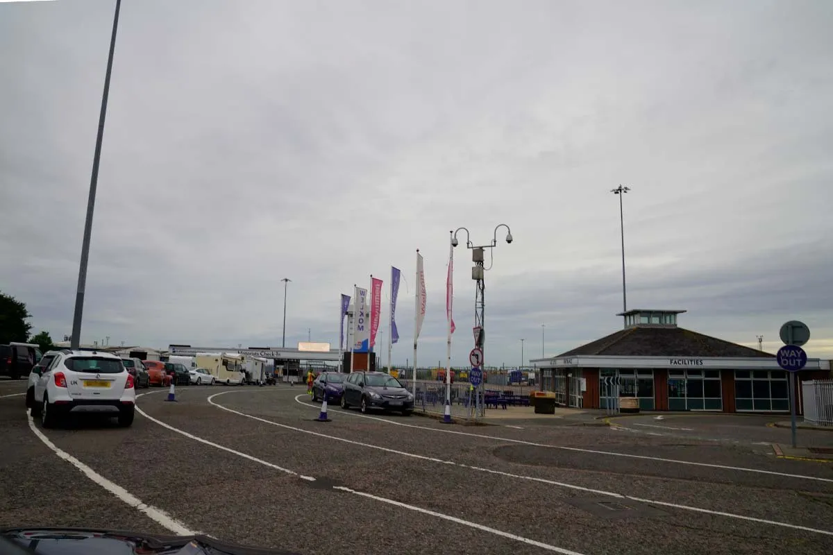 Autos in der Warteschlange auf dem Stellplatz von Harwich International, mit den Flaggen von Stena Line und einem flachen Gebäude mit der Aufschrift Facilities