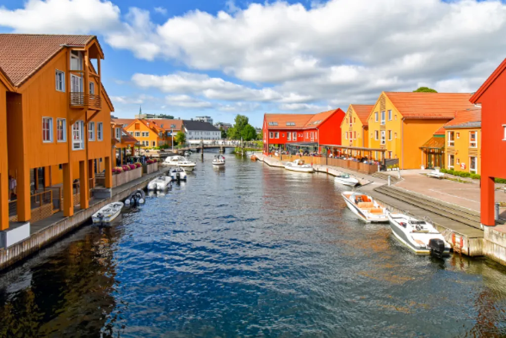Orange und rote Holzhäuser am Wasser in Kristiansand, mit kleinen Motorbooten am Kai unter einem blauen Himmel mit Wolken