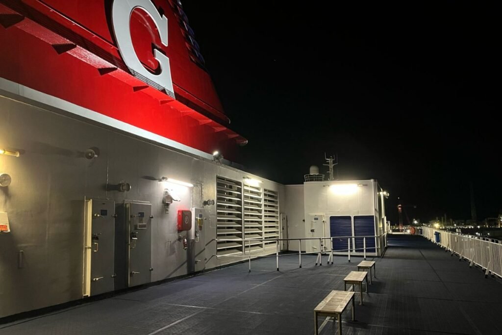 Das leere Oberdeck der Fähre bei Nacht, mit dem roten Schornstein mit einem großen weißen G und Holzbänken unter den Lampen