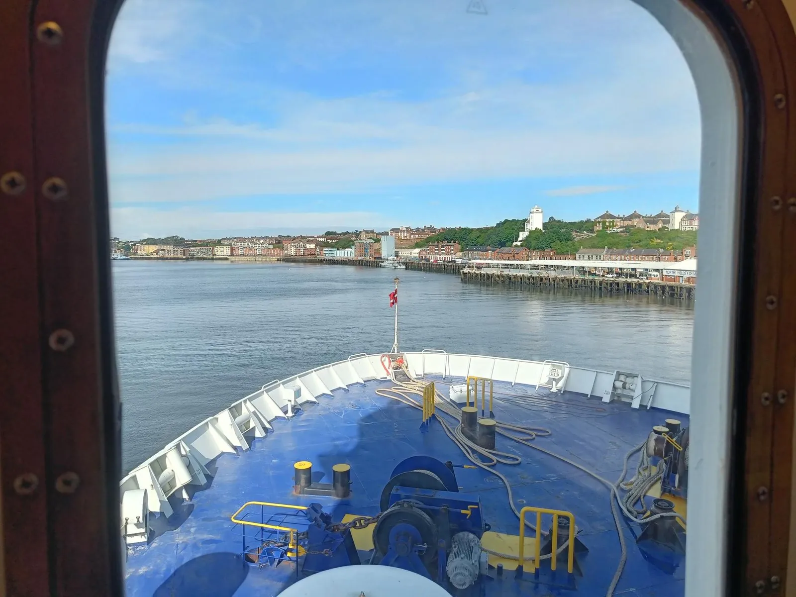 Blick durch das Kabinenfenster über den blauen Bug, beim Einlaufen auf der Tyne an der Kaimauer von North Shields entlang