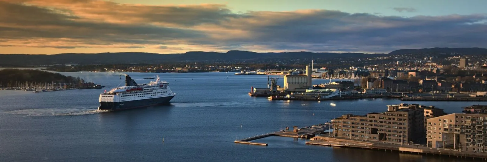Eine Fähre fährt bei Sonnenuntergang in den Oslofjord, rechts die Stadt