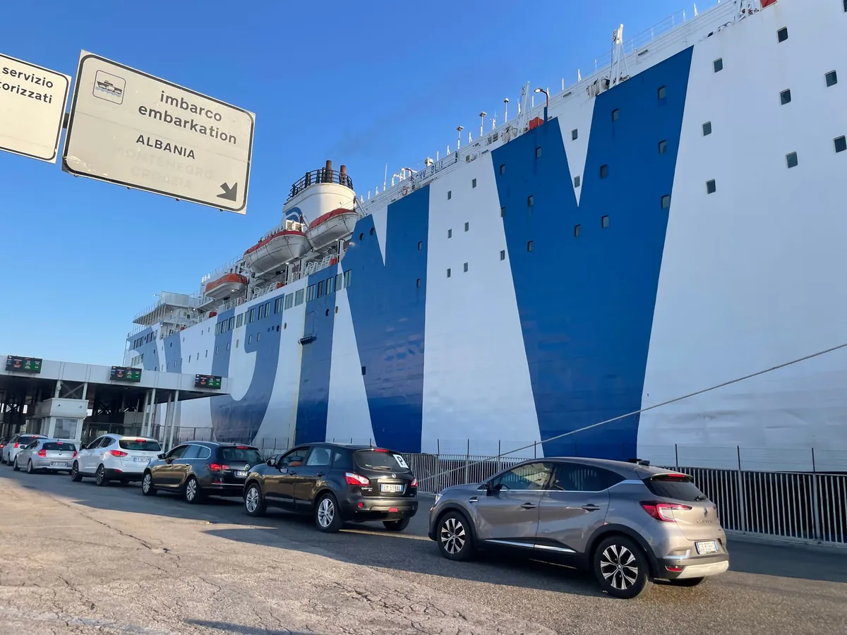Autos in der Warteschlange zum Einschiffen im Hafen von Bari, unter einem Schild mit imbarco embarkation Albania, neben einem großen weiß-blauen Schiff von GNV