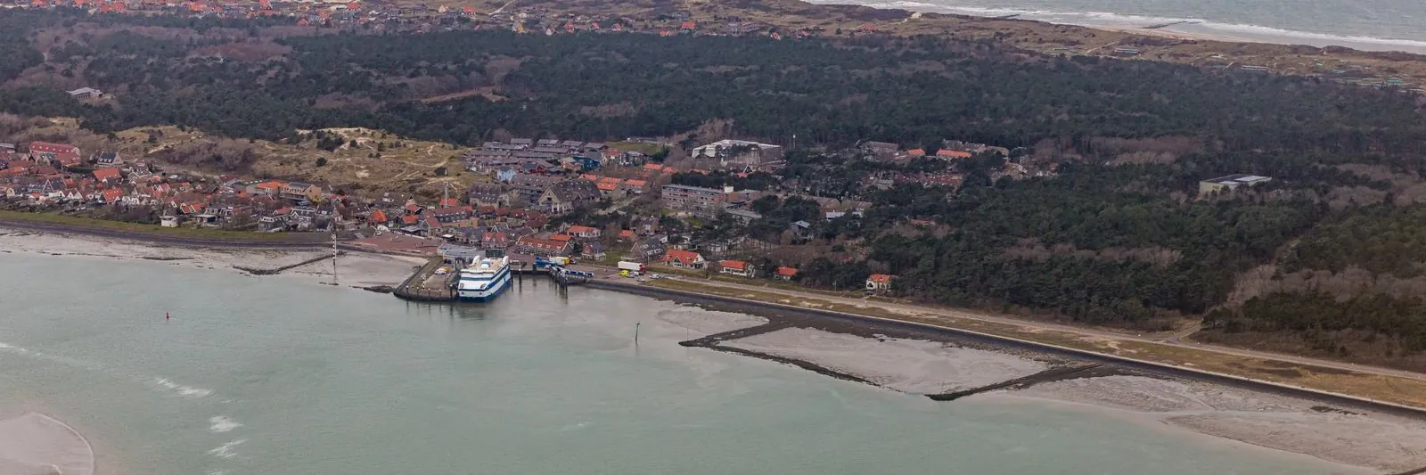 Vlieland aus der Luft: die Fähre am Anleger, dahinter das Dorf, Wald und Dünen