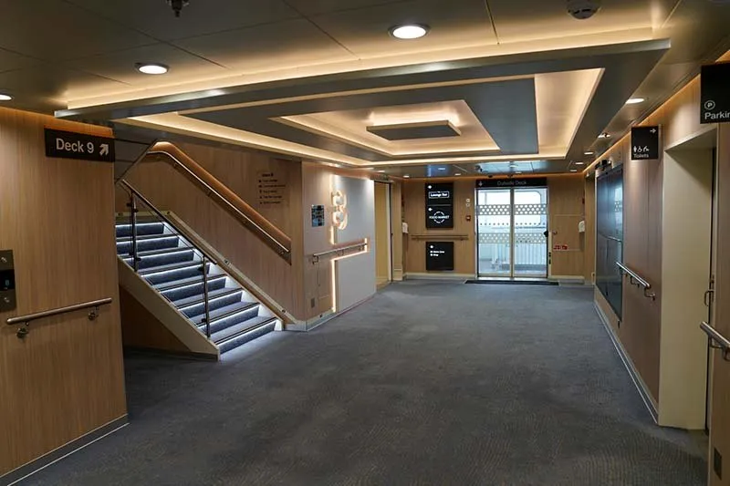 Treppenhaus an Bord von P&O Ferries mit Holzwänden, einem Schild zu Deck 9 und Glastüren zum Außendeck