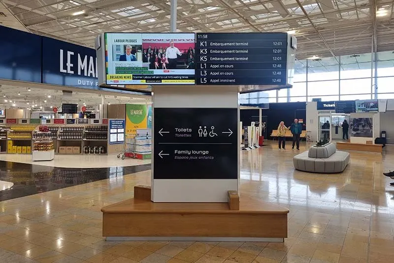 Abfahrtstafel im Terminal mit den Zugnummern K1 bis L5 und den Meldungen embarquement terminé und appel en cours, neben einem Duty-free-Laden