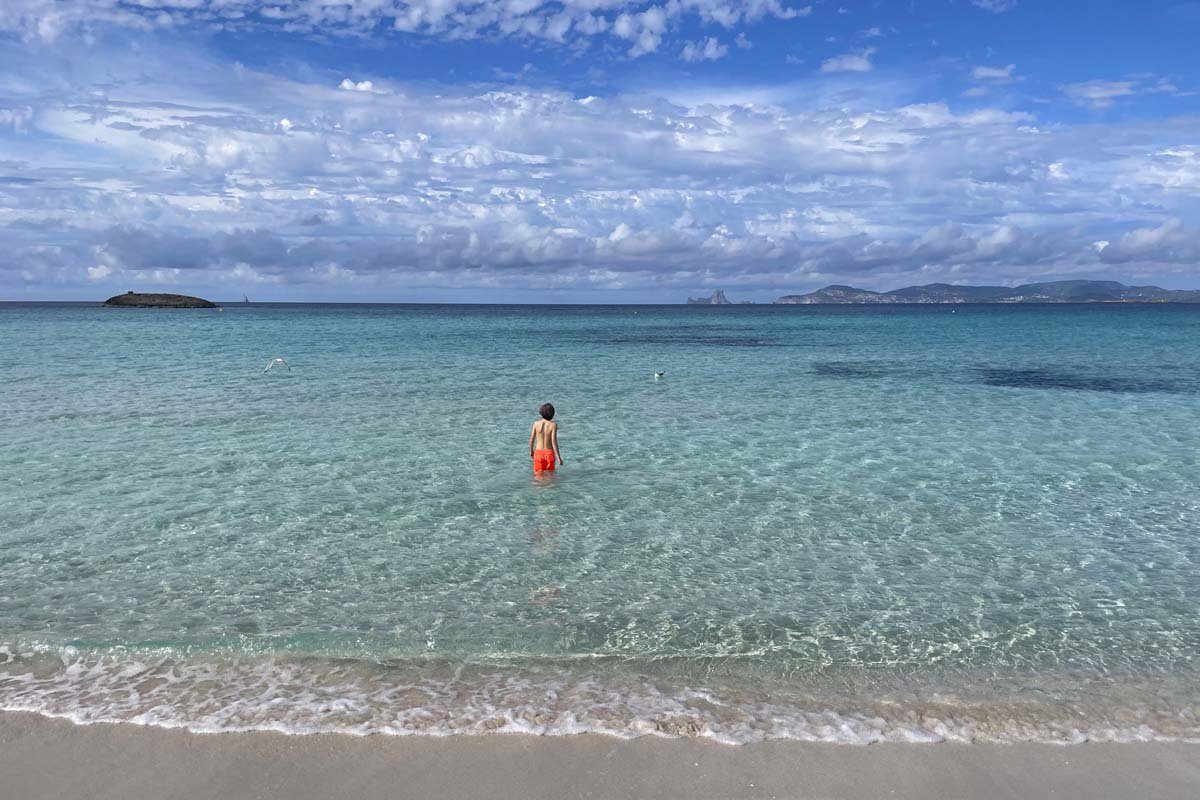 Flaches, klares Meerwasser am Strand, ein Kind steht bis zu den Knien im Meer