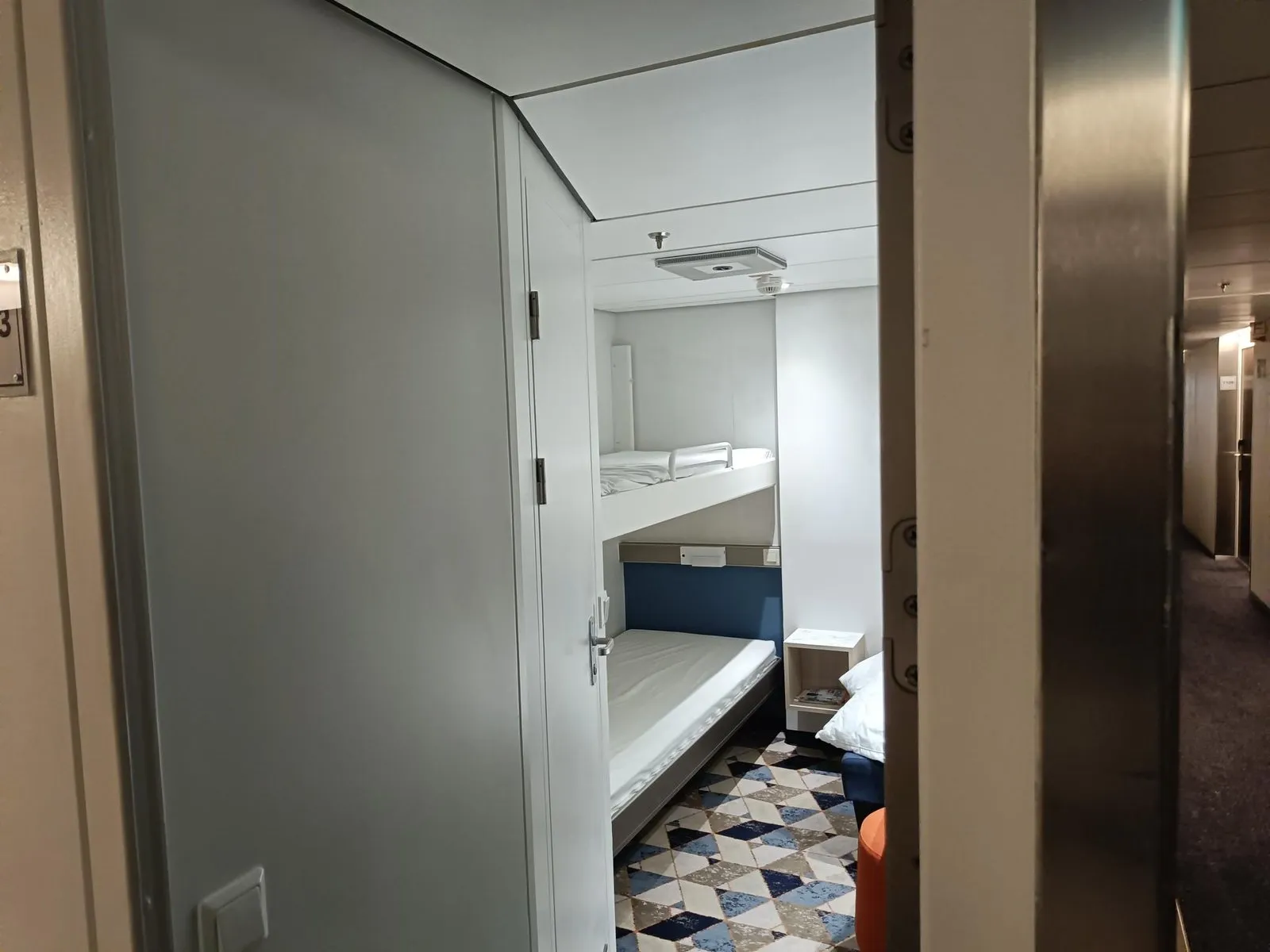 Blick durch die offene Kabinentür auf ein Etagenbett, mit einem ausklappbaren Gitter am oberen Bett