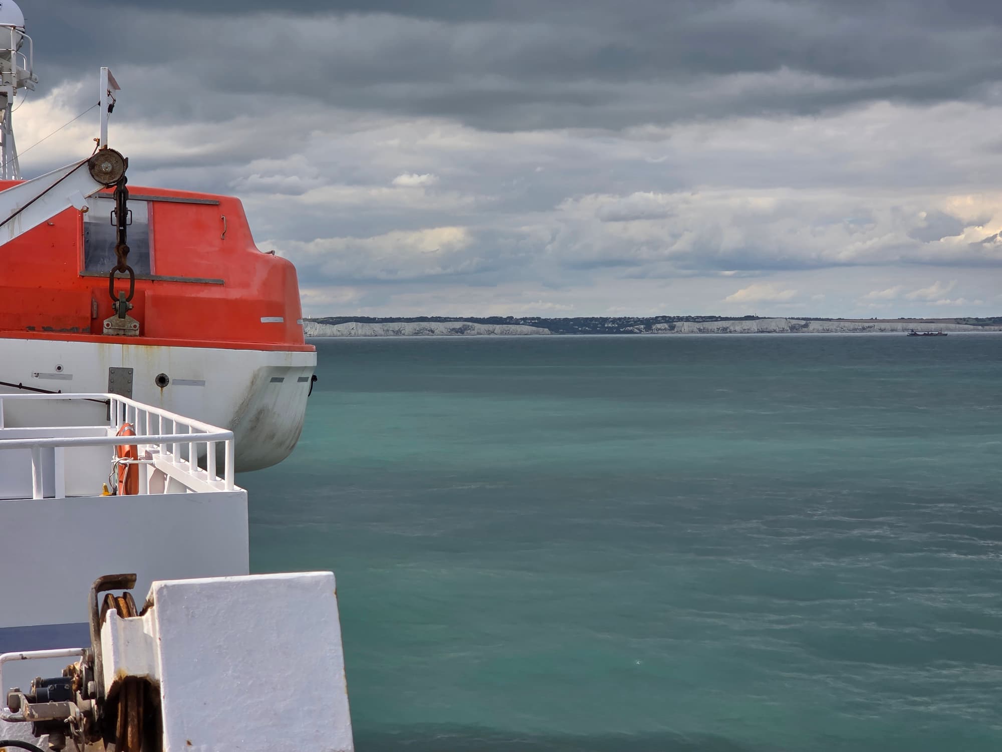 Ein orangefarbenes Rettungsboot mit Rost an der Reling der Delft Seaways, in der Ferne die weißen Klippen der englischen Küste