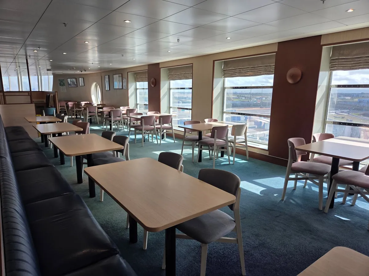 Ein Restaurant mit Holztischen, Stühlen und großen Fenstern an Bord der Delft Seaways