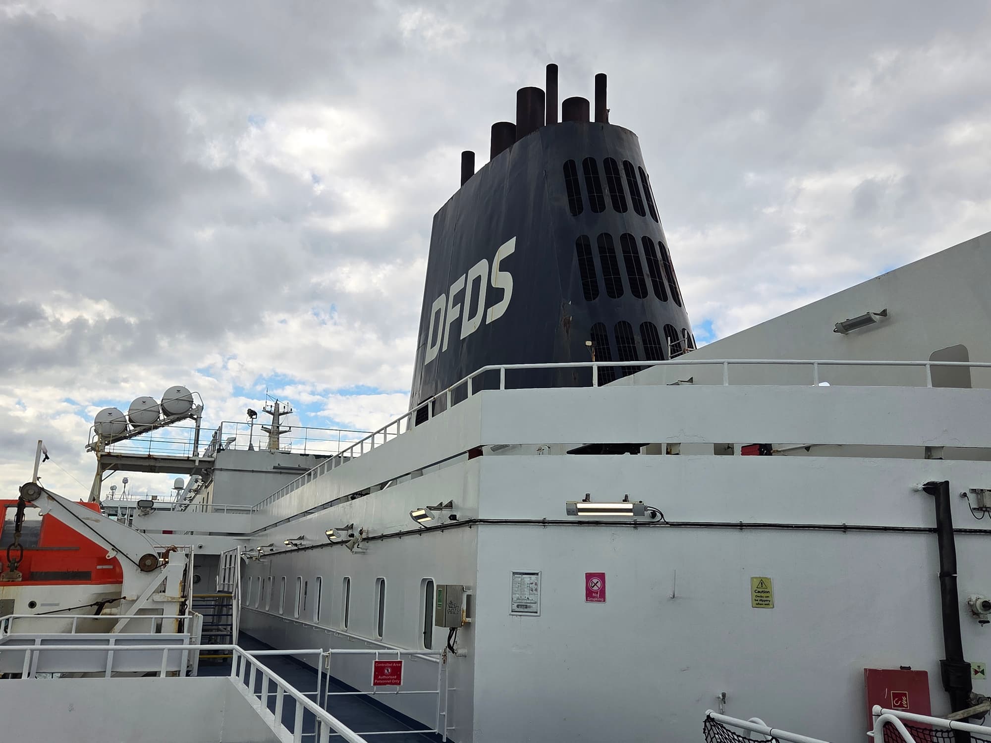 Der schwarze DFDS-Schornstein und das Außendeck der Delft Seaways unter bewölktem Himmel, daneben die Rettungsboote